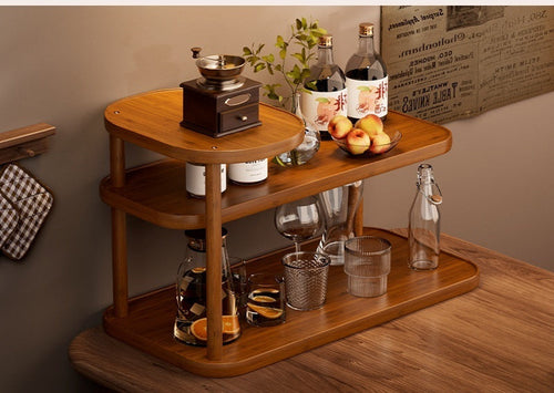 Three-tier bamboo countertop shelf standing on a wooden counter, its open tiers holding glassware and a carafe