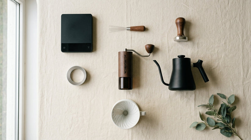 Editorial flatlay of seven essential home barista tools arranged geometrically on cream linen