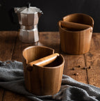 Two acacia knock boxes on a wooden counter beside a moka pot and coffee beans
