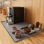 Black food-grade silicone barista mat with raised edges catching coffee grounds