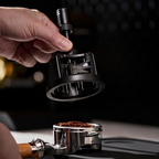Hand holding the TrueShih Vertical Needle Distributor above a filled portafilter during espresso prep