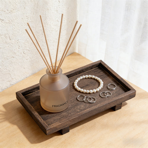 Footed solid wood tray holding a frosted reed diffuser and a pearl bracelet