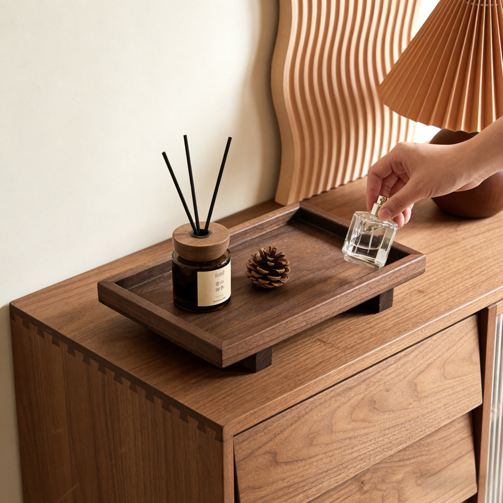 Dark wood tray on a walnut cabinet with a reed diffuser and a pinecone